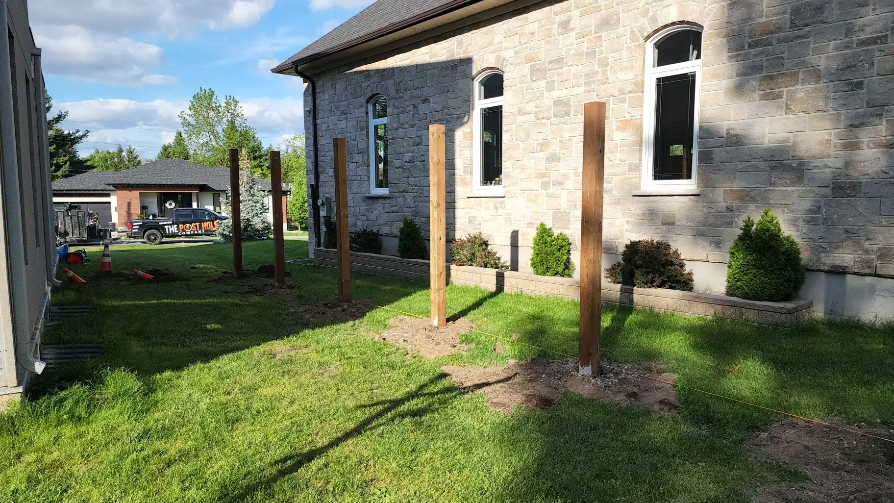 fence posts aligned, level and plumb to a string line in between 2 homes with The Post Hole Company truck in the background parked on the street.