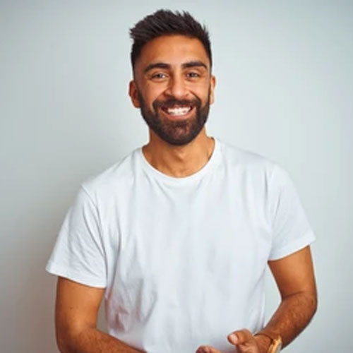 Raj Patel, a dedicated digging and building operator for The Post Hole Company, poses against a neutral grey backdrop, wearing a white t-shirt. His confident demeanour reflects his expertise and readiness for construction work.